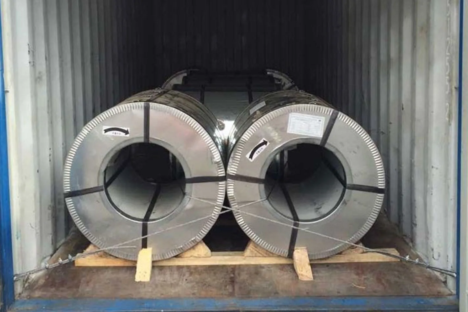 Steel coils secured with wooden blocking and bracing inside a shipping container for safe transport.